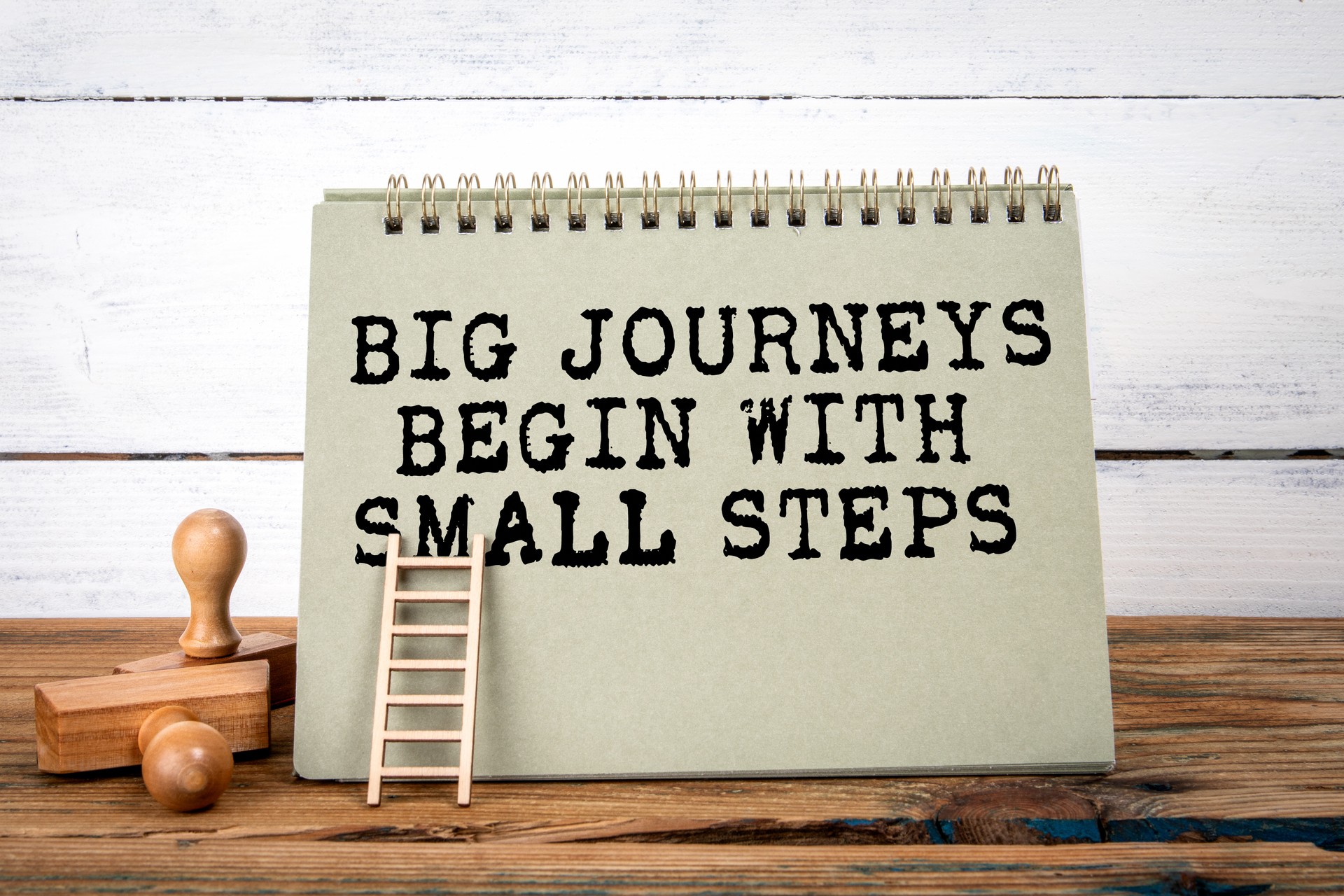 Big Journeys Begin With Small Steps. Green notepad on wooden texture table and white background